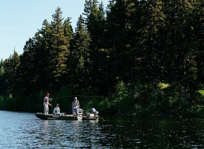 Three anglers in a boat with one casting into the waters of Roche Lake, located near Kamloops, BC.