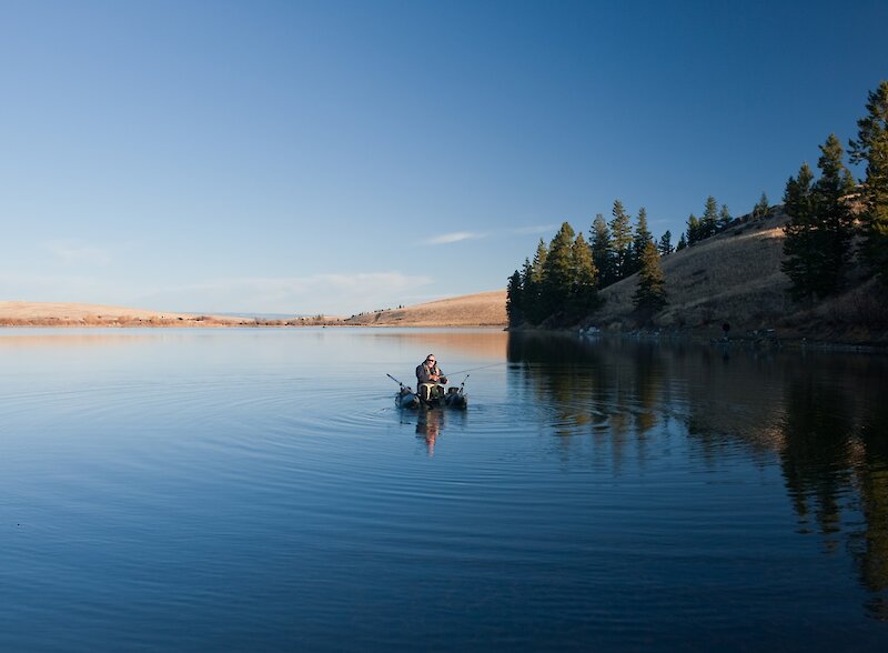 Angler fishing from an inflatable boat on Edith Lake with grasslands and trees in the background near Kamloops, BC.