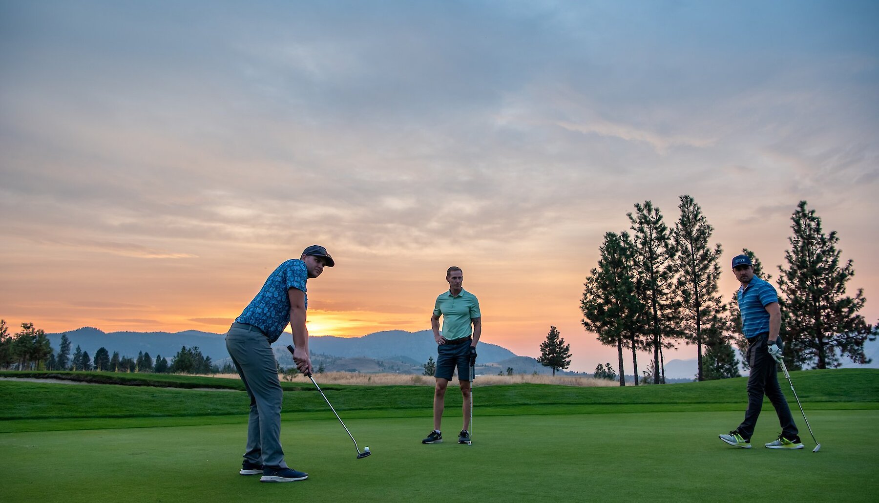 Three golfers line up on a golf green at sunset.