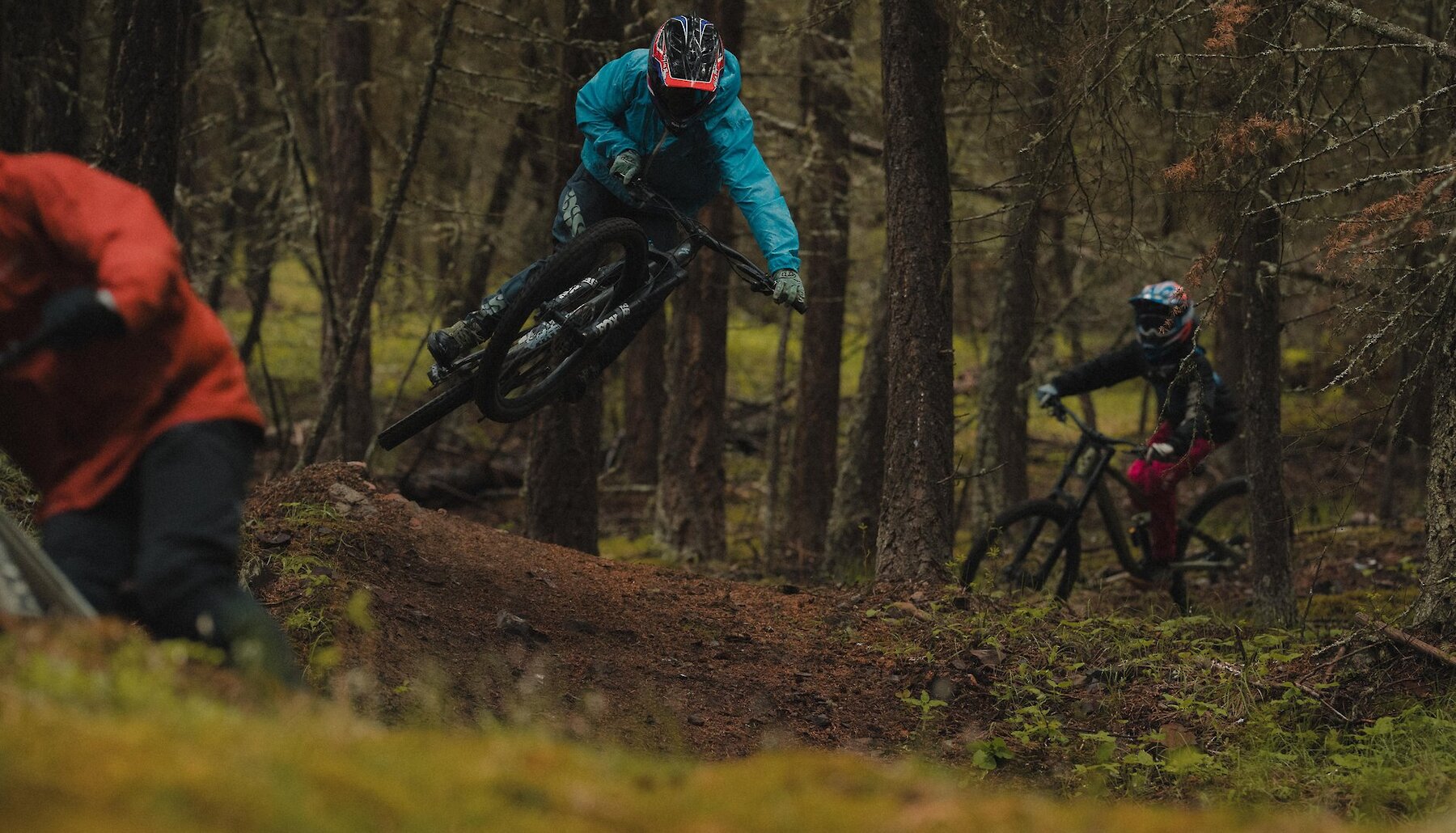 A group of riders with one rider launching off a jump on a mountain bike through the trails at Harper Mountain near Kamloops, BC.