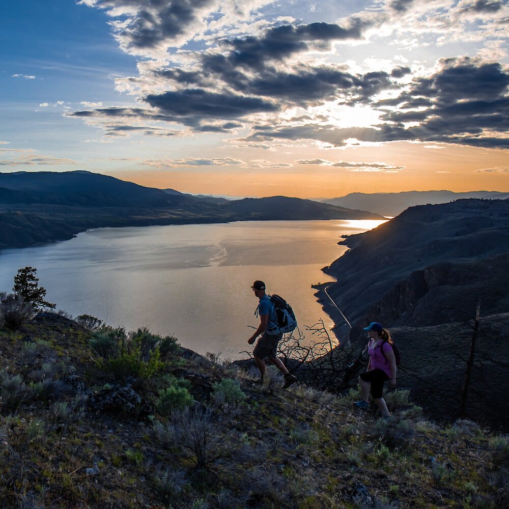 A couple going for a walk at Battle Bluff with the view of the sunset over Kamloops Lake.