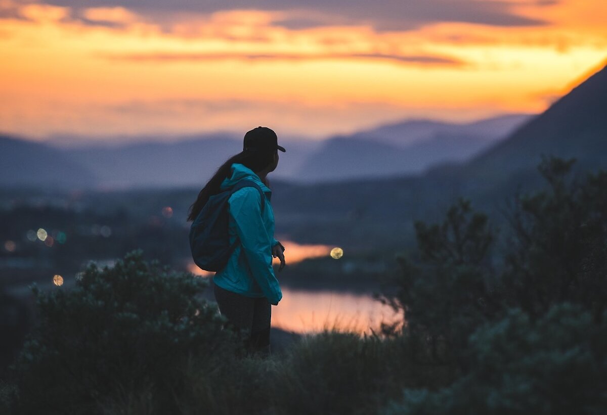 A woman look back over her shoulder at the scenic Kamloops sunset over Kamloops lake and the mountains.