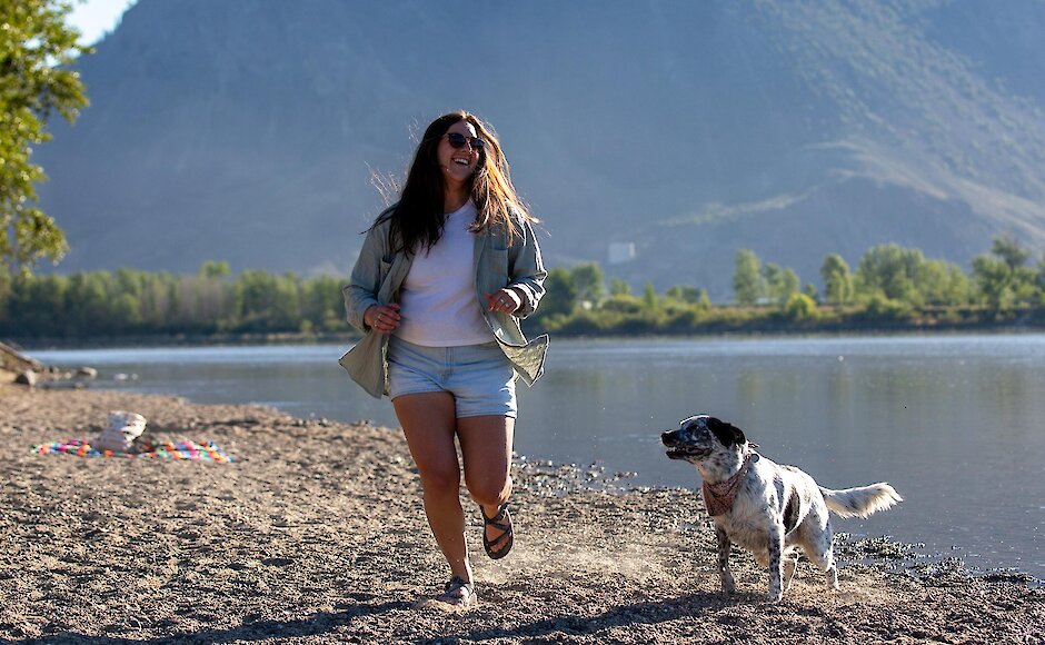 Woman running along side her dog at a Overlander beach in Kamloops, BC.