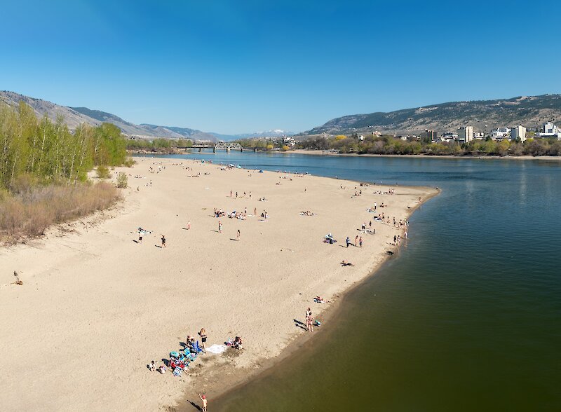 Wide sandy beach at Overlander Park with people relaxing along the North Thompson River.