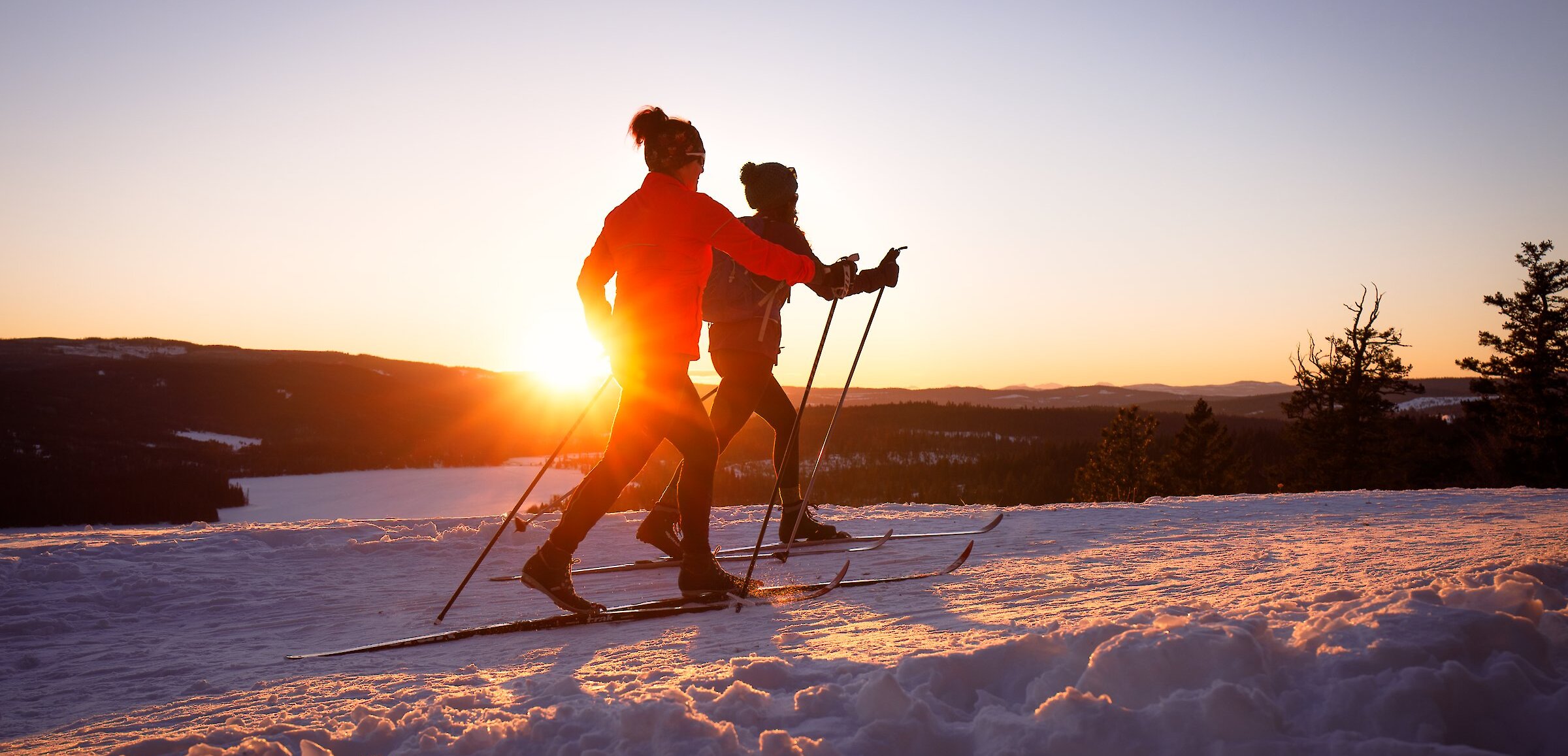 Two cross country skiers gliding on the trails at Stake Lake with the sunset in the background located near Kamloops, BC.