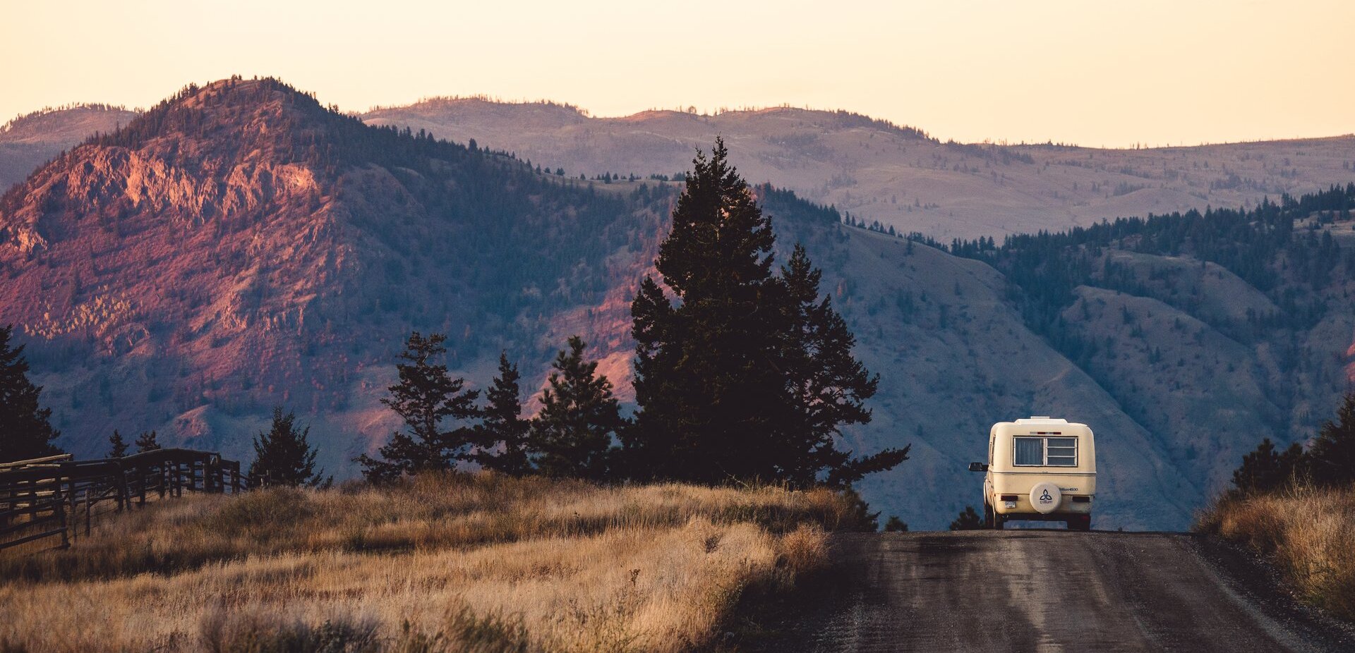 A truck pulling a camping trailer down a dirt road with scenic mountains in the background near Kamloops, BC.