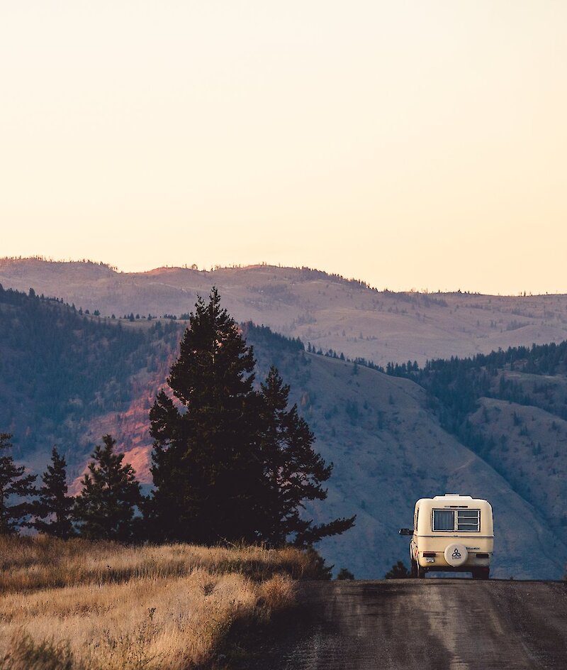 A truck pulling a camping trailer down a dirt road with scenic mountains in the background near Kamloops, BC.