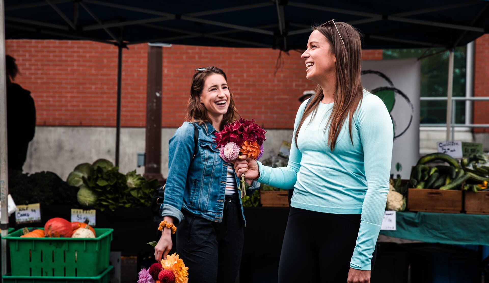Two women laughing holding their bouquets of flowers from the Kamloops Farmers Market.